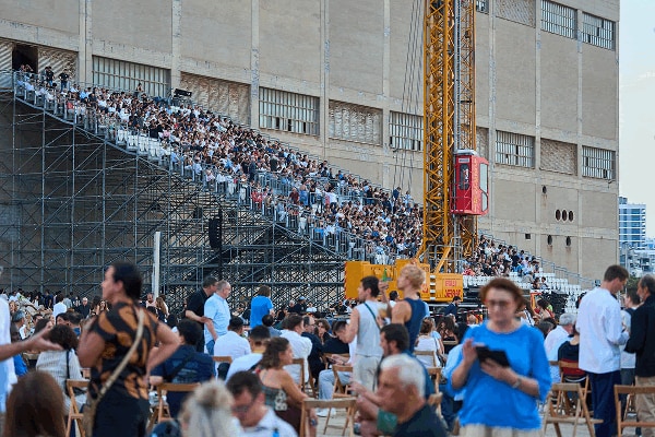 Crowd seated on temporary scaffolding outside the Three Chimneys power plant for the UIA 2026 opening.